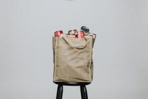 Reusable grocery bag filled to top with groceries, sitting on a stool.