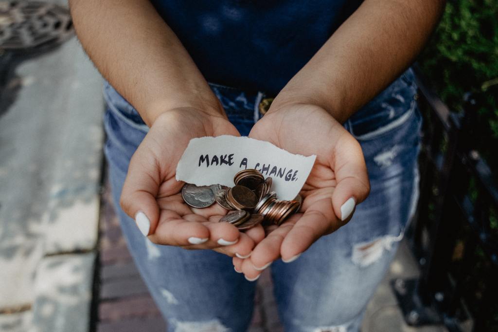 Woman's hands, holding United States currency coins, and a note that says 'make a change"
